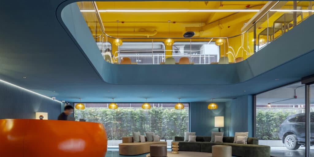 ردهة فندق Vela be Siam بتصميم داخلي نابض بالحياة، مع مكتب استقبال برتقالي وخلفية خضراء.