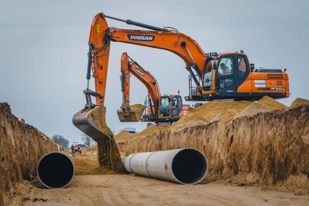 Excavators installing large-diameter pipelines along a trench, showing construction progress.