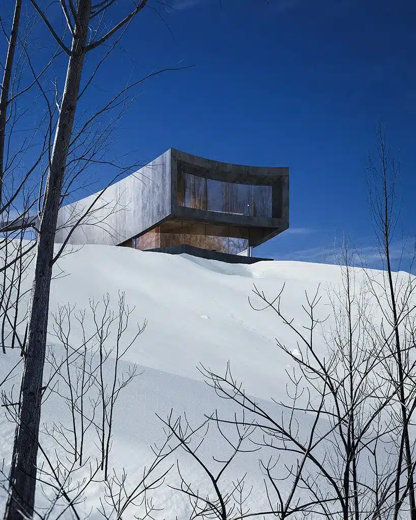 مبنى معدني بواجهة زجاجية يطل على منحدر ثلجي حاد في يوم صافٍ.