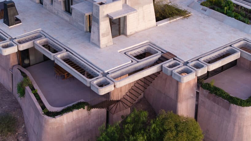 صورة جوية للسقف المسطح للمنزل الخرساني في مندوزا، مع وجود سلالم خارجية، مناطق مفتوحة، وفتح بيئية تسمح بدخول الضوء إلى المستويات السفلى.
