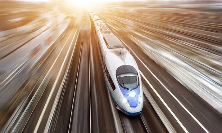 A high-speed train speeding along a modern rail track, illuminated by sunlight, symbolizing rapid urban development and advanced transportation in Riyadh.