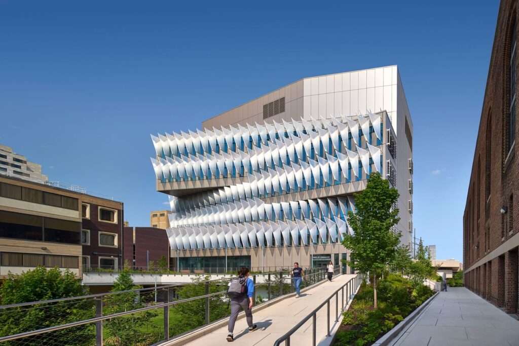 The Vagelos Laboratory for Energy at UPenn, showcasing its modern architectural design with a dynamic ETFE sunshade facade, pedestrians walking along a landscaped walkway under a clear blue sky.