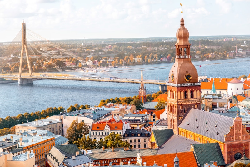 An aerial view of Riga, Latvia, showcasing the iconic St. Peter&rsquo;s Church and Van&scaron;u Bridge, with historic rooftops and riverfronts in the background &mdash; symbolizing the blend of heritage and modern development driven by the Rail Baltica project