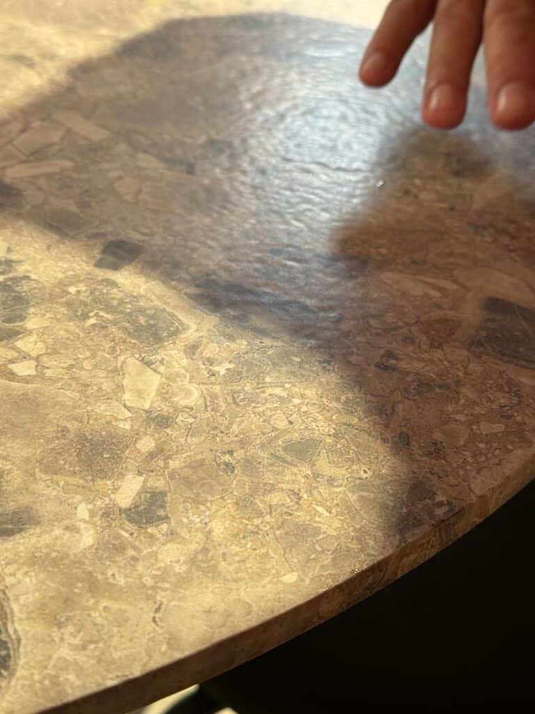 Round marble surface with natural texture showcased at Cersaie 2025, with a hand touching the stone to highlight its quality.