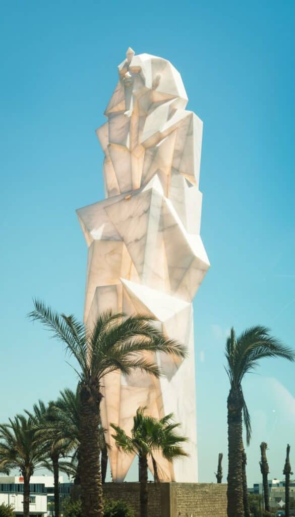 Side view of the monumental pharaonic-inspired statue along the Cairo&ndash;Alexandria Desert Road, framed by palm trees and passing traffic.