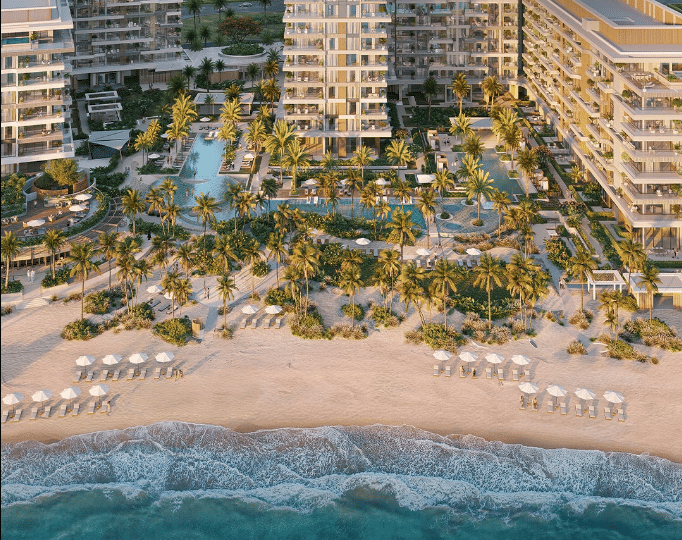منظر جوي للمنطقة الساحلية في سوتو غراندي بألمحرا، يظهر شاطئ رملي نظيف، ومياه زرقاء صافية، ونخيل كثيف، وحمام سباحة كبير محاط بكراسي شمسية وأكواخ مظللة.
