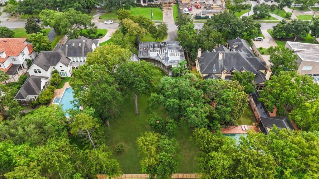 Aerial view of a lush, upscale Houston neighborhood with large homes nestled among mature trees, private pools, and winding paved streets.