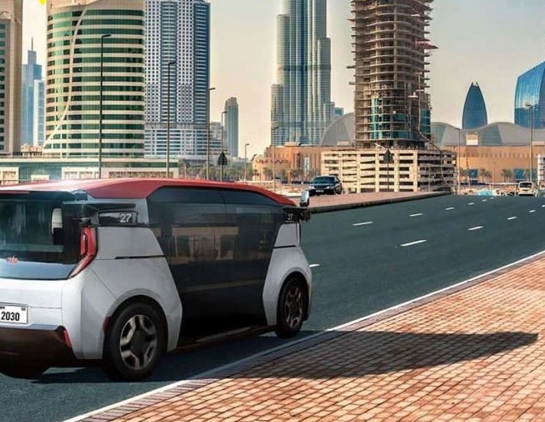 A futuristic white and red autonomous pod glides along a quiet Dubai highway, with the city&rsquo;s iconic skyline &mdash; including Burj Khalifa and under-construction towers &mdash; rising behind it.