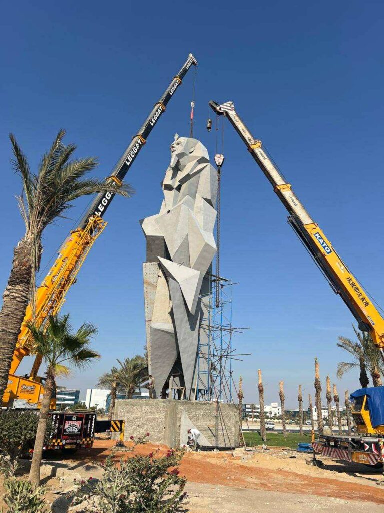 Installation works of the modern pharaonic statue with cranes at the Grand Egyptian Museum during daylight.