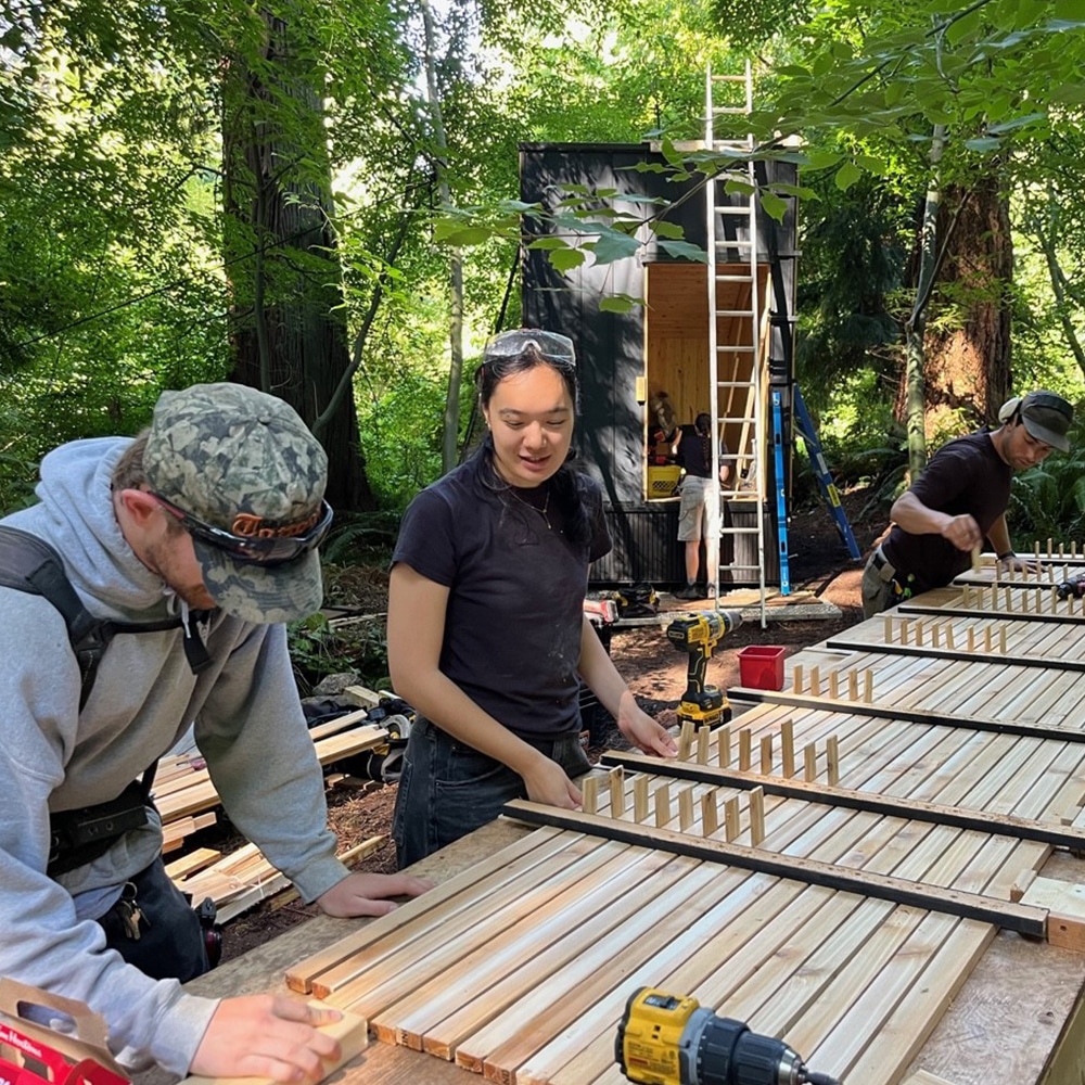 People assembling wooden panels at a small construction site in the forest