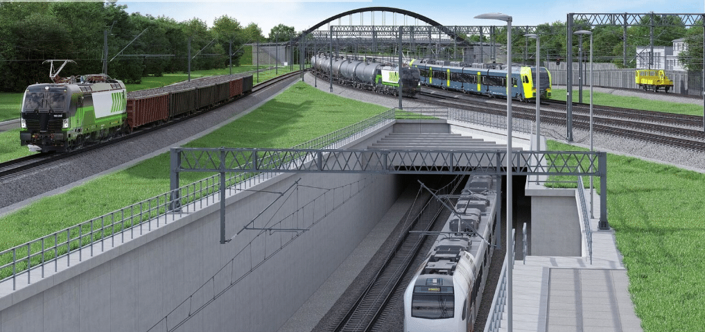 A 3D visualization of the Maksymilianowo railway upgrade, showing a freight train passing over an elevated track while a passenger train travels beneath it through a tunnel. A pedestrian bridge and multiple rail levels are visible, highlighting modern rail infrastructure design.