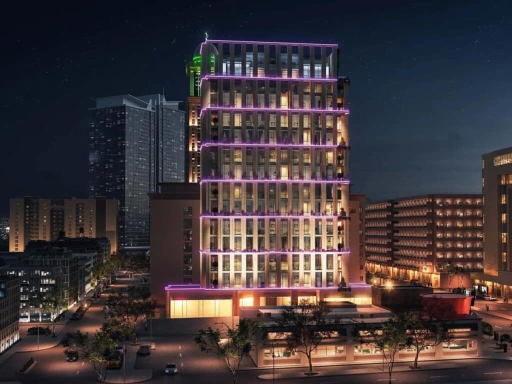 The Rise&rdquo; tower in Riyadh at night, glowing with soft purple and warm yellow lighting against a starry sky, standing out among surrounding buildings with quiet streets and gentle urban life below.