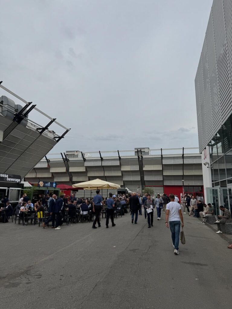 A woman gently touches a large porcelain tile on display at Cersaie 2025, holding a microphone in one hand &mdash; likely explaining its texture, finish, or technology to an audience. A small label reads &ldquo;Safe Technology,&rdquo; hinting at innovation beneath the surface.