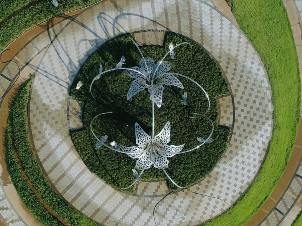 Stainless steel sculpture 'Flowers and Butterflies Dance' reflecting sunlight and surrounding flowers in Taichung, Taiwan