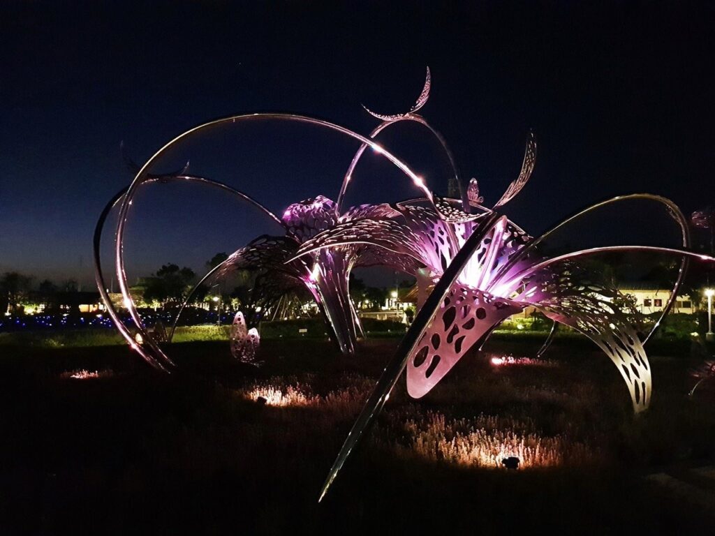 Stainless steel sculpture 'Flowers and Butterflies Dance' reflecting sunlight and surrounding flowers in Taichung, Taiwan