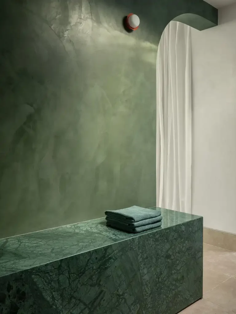 A green marble bench beside a matching wall, with folded towels and a soft white curtain.