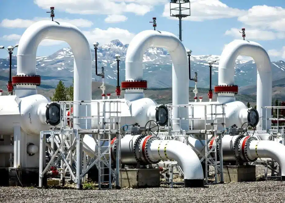 Large white hydrogen pipelines at a green energy facility, with snow-capped mountains in the background under a clear blue sky &mdash; symbolizing modern clean energy infrastructure.