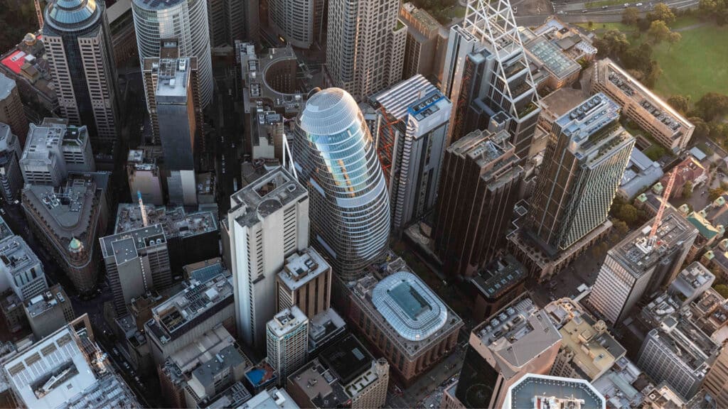Aerial view of 1 Elizabeth Tower in Sydney’s CBD, its curved glass facade glowing in golden hour light among surrounding skyscrapers.