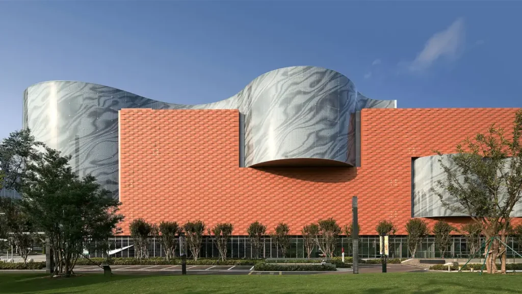 Chengnan’s facade — warm terracotta walls meet flowing, wave-like glass under a clear blue sky.