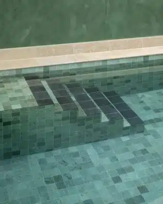 a pool&rsquo;s mosaic tiles in green and black, with a light stone coping.