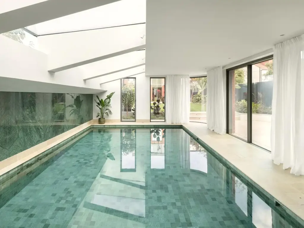 An indoor pool with green mosaic tiles, reflecting natural light from skylights and large windows.