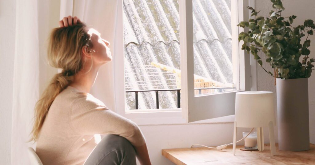 Woman soaking in morning sun by her window, peaceful room.