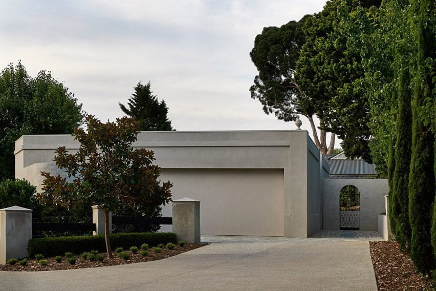 منزل بواجهة خرسانية صامتة، مع مدخل قوس وحديقة منظمة.