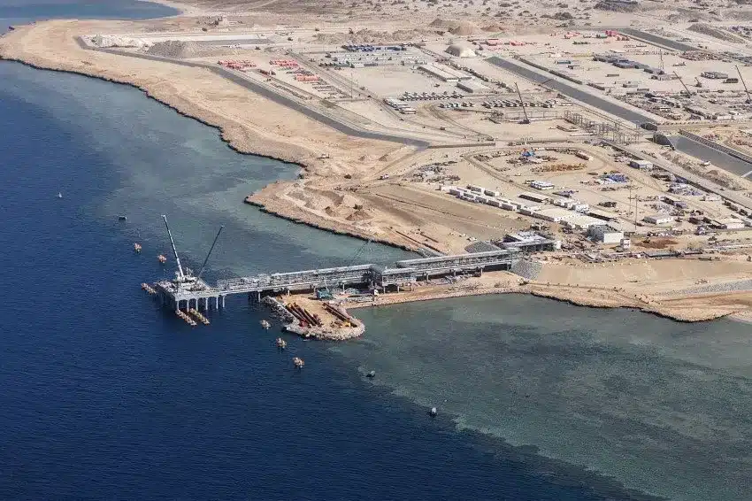 Aerial view of a massive coastal industrial project on the Red Sea, featuring a construction underway pier, pipelines, and processing units &mdash; showcasing the expansion of clean energy infrastructure in a desert landscape.