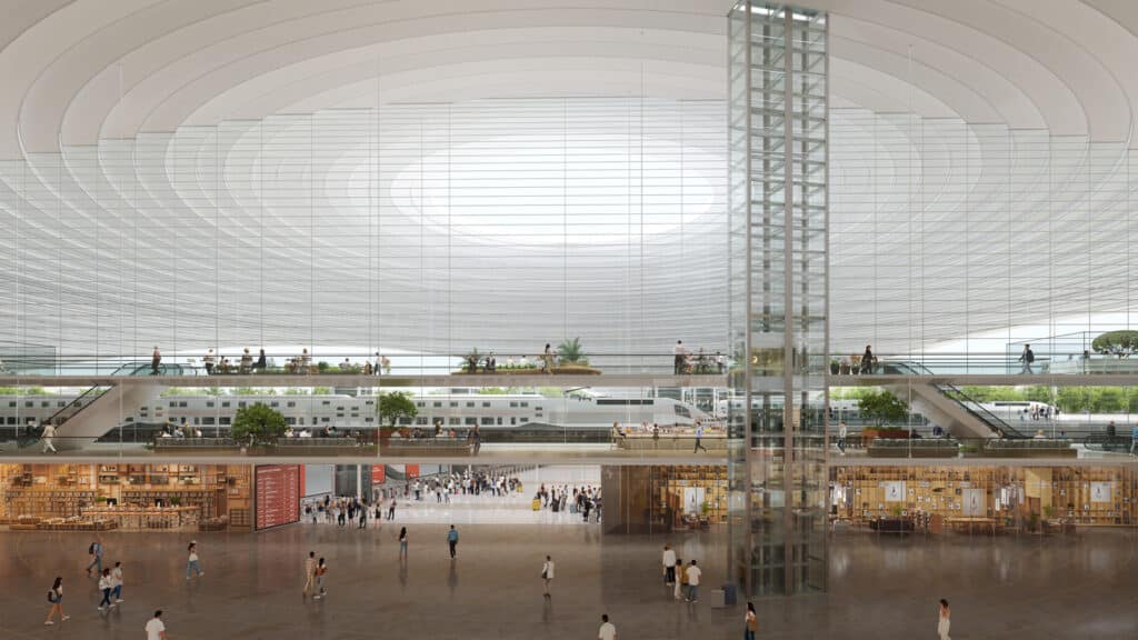 The spacious interior of Casablanca&rsquo;s new Casa Sud Station, showing sleek high-speed trains on the upper level, surrounded by multi-story public spaces with cafes, bookshops, and seating areas &mdash; all under a dramatic curved ceiling that floods the space with natural light.