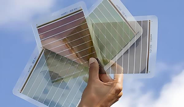 يد تمسك ثلاث ألواح شمسية شبه شفافة أمام سماء زرقاء صافية، تُظهر ألوانها المختلفة وتصميمها الرقيق والعصري.