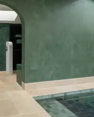 A soft green textured wall beside a pool with green tiles and light stone flooring.