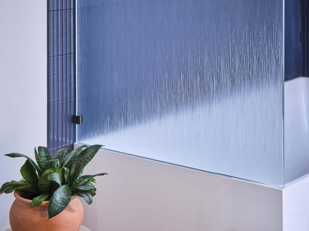 Frosted glass panel with linear texture in a modern bathroom, potted plant nearby.