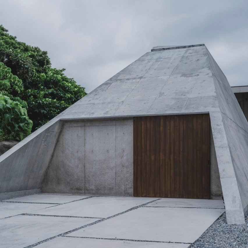 منزل خرساني مائل بباب خشبي داكن، يبرز في منظر طبيعي.