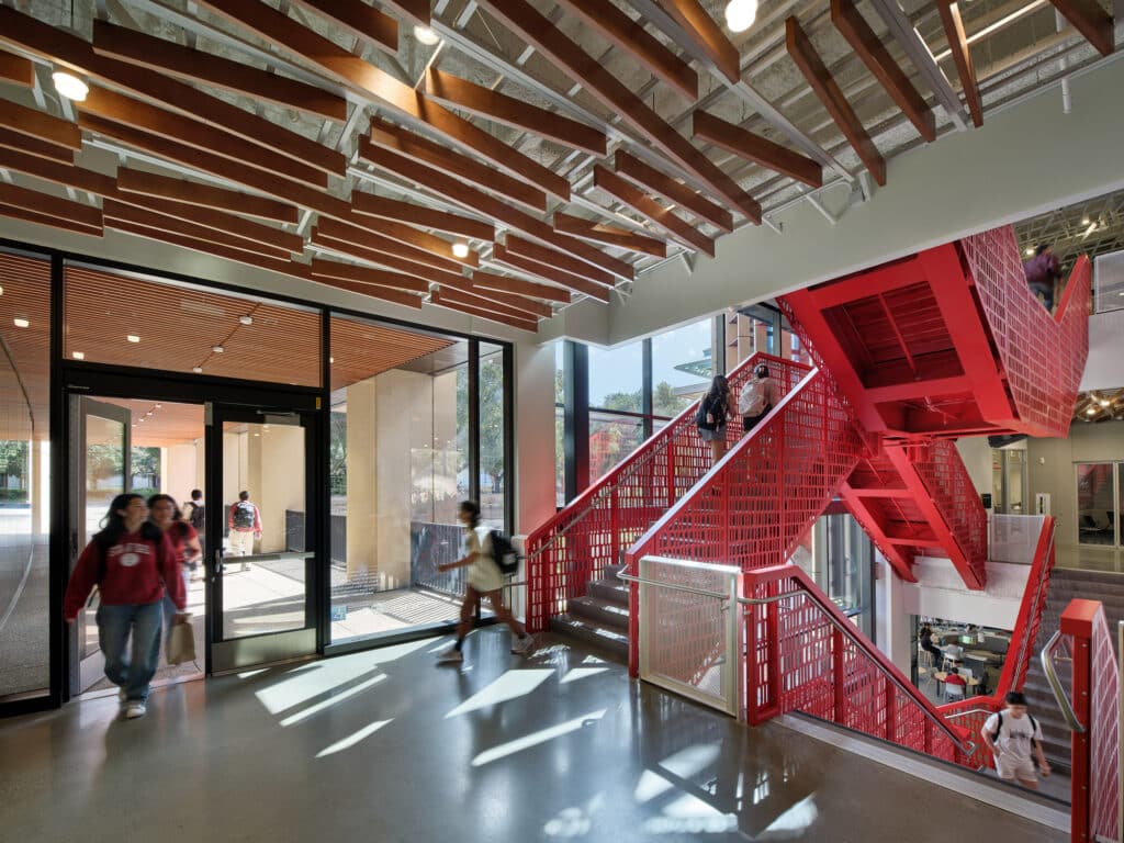 Inside Stanford&rsquo;s new building: bold red staircase, wooden ceiling slats, students moving between floors.
