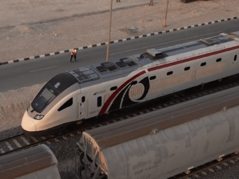 A sleek Etihad Rail passenger train glides along desert tracks, with a worker in a safety vest nearby capturing the real-world launch of UAE&rsquo;s first high speed rail service amid vast, open landscapes.