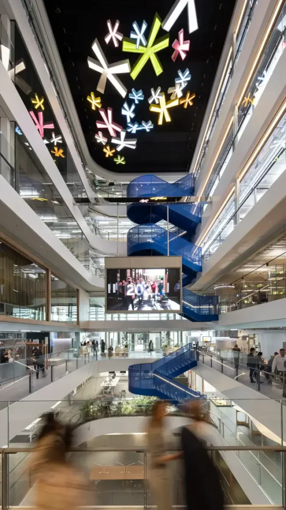 A soaring atrium in 1 Elizabeth Tower, featuring a vibrant blue spiral staircase and a ceiling of glowing star-like lights, with people moving through the modern, multi-level space.