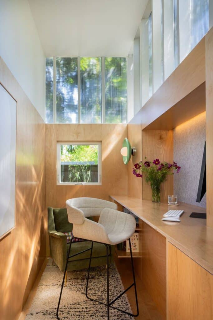 مكتب مشرق بألواح خشبية، ومكتب طويل، وكراسي مريحة، ونوافذ كبيرة تطل على الأشجار.