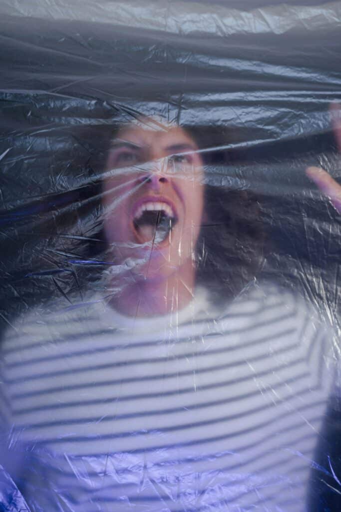 امرأة تصرخ خلف طبقة من الغلاف البلاستيكي المتجعد، وجهها مشوه وكأنه محبوس في صرخة صامتة.