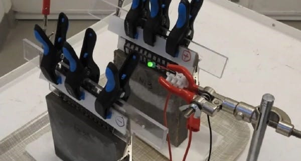 عينة خرسانة مثبتة في جهاز اختبار مع أسلاك وأضواء إلكترونية.