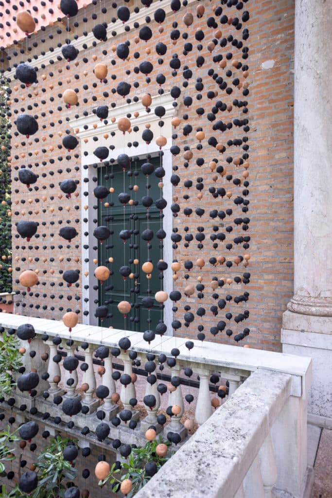 مبنى من الطوب يُغطّى بسلسلة من الكرات المعلقة السوداء والبيج، كأنه يرتدي حجابًا من الظلال تحول مؤقت يمزج بين العمارة والفن.