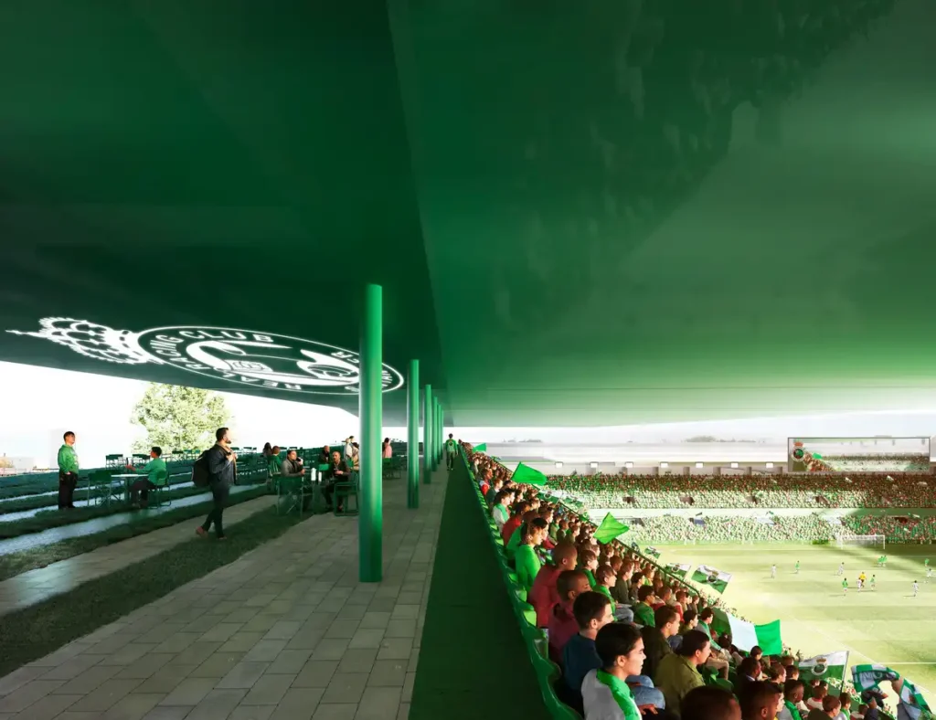 Inside the renovated El Sardinero Stadium — fans sit in green seats under a massive green roof, with the club’s logo projected overhead. The pitch is alive with players and a sea of supporters under bright daylight.