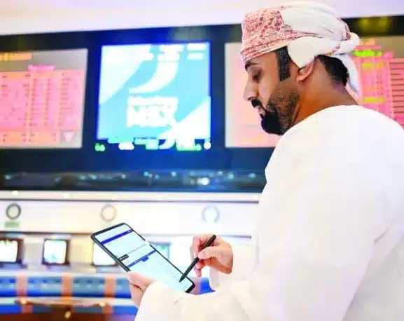 رجل بالزي العماني التقليدي يراجع بيانات احتجاز الكربون على جهاز لوحي، وخلفه شاشات تُظهر مؤشرات الطاقة في الوقت الفعلي.