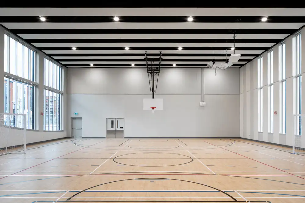 Bright, empty gym at CRJDA Sainte-Thérèse with wood floors, big windows, and basketball hoop.