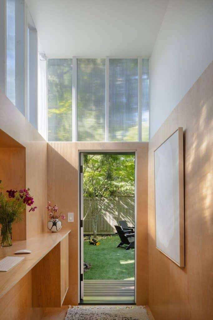 A sleek, wood-lined office with a glass door opening to the green backyard.