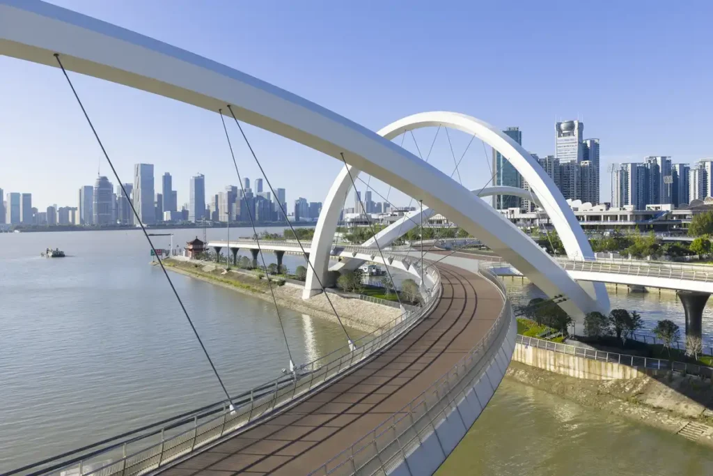 Close-up of the Grand Canal Gateway Bridge’s pathway — white arches flowing over water, framed by Hangzhou’s modern skyline under a clear blue sky.