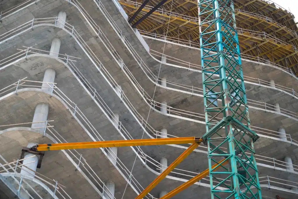 منظر من أسفل لبناية خرسانية قيد الإنشاء مع سقالات وأعمدة ورافعة زرقاء.