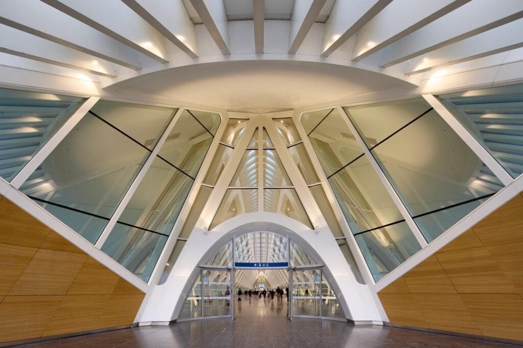 Modern interior entrance of Mons station — white geometric arch with glass panels and wood accents.