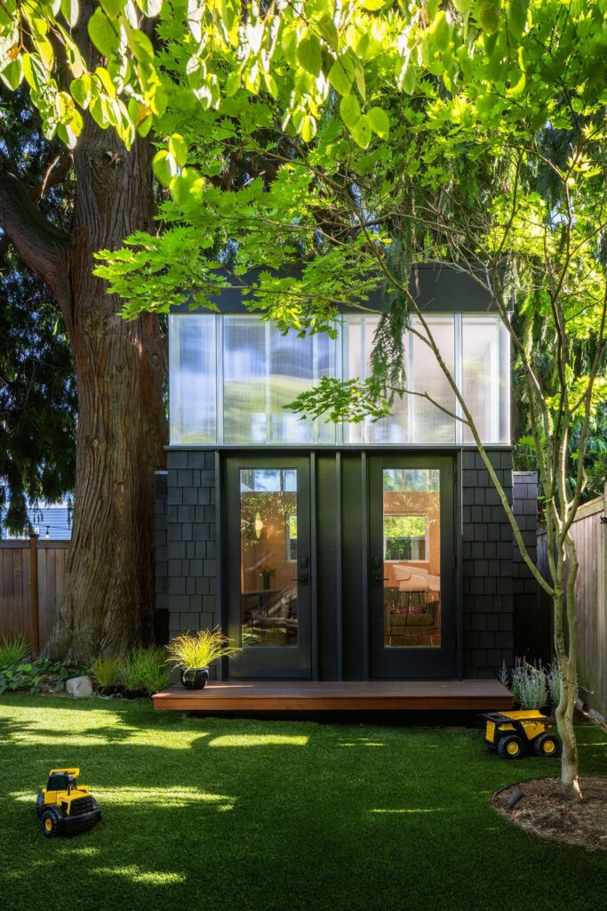 مبنى حديث بألواح سوداء وأبواب زجاجية، مُحاط بشجرة كبيرة في فناء مشمس.