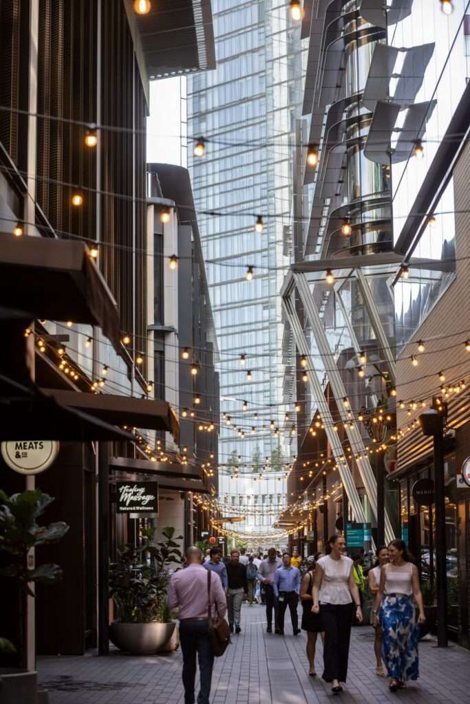 Barangaroo&rsquo;s lively laneway: people stroll under string lights between modern buildings and boutique shops.