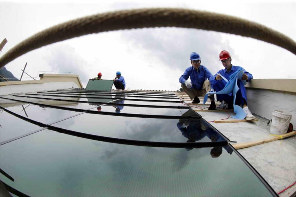 Workers installing reflective glass panels on a rooftop.